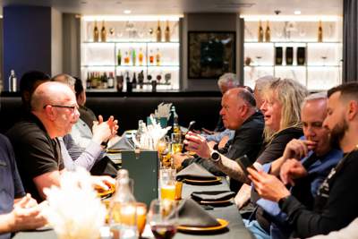 A group of men sit around a long table in a restaurant and engage in lively conversation.