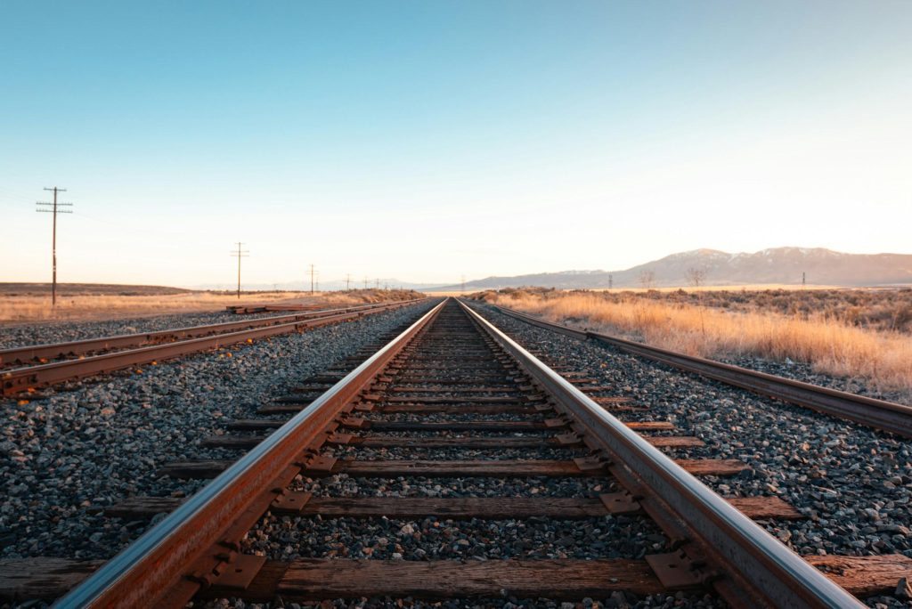 A pair of railway tracks stretching toward the distant horizon under a clear, open sky.
